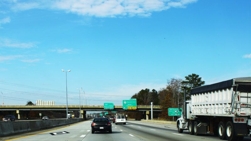 Cars on an interstate highway, with green signs in the distance.