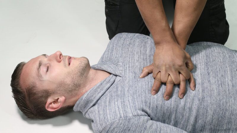 An unconscious man receives CPR from an unseen person.