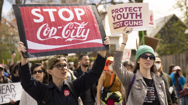 A protester holds up a sign reading "STOP Cop-City" stylized like the Coca-Cola logo.