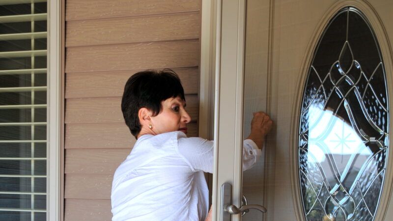 An older woman knocks on a residential door.