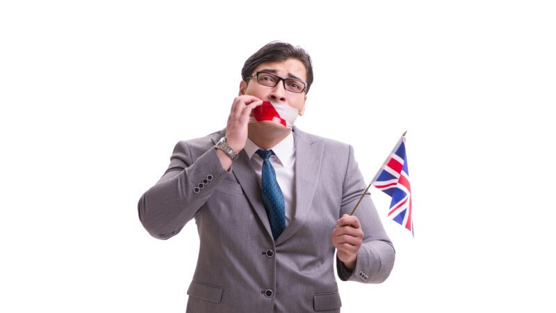 A businessman with tape over his mouth holding a flag of the United Kingdom. | Elnur | Dreamstime.com