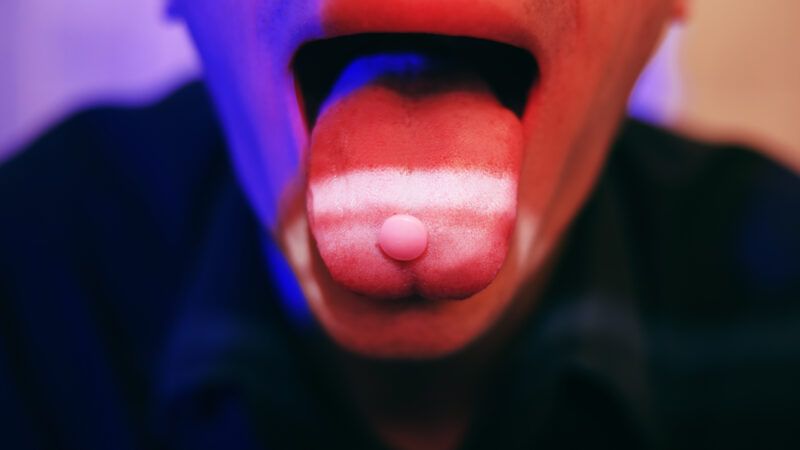 A neon tinted person with an open mouth holds pills on their tongue | Photo 177051537 © Olha Karpovych | Dreamstime.com