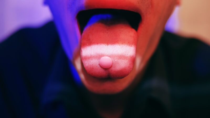 A neon tinted person with an open mouth holds pills on their tongue