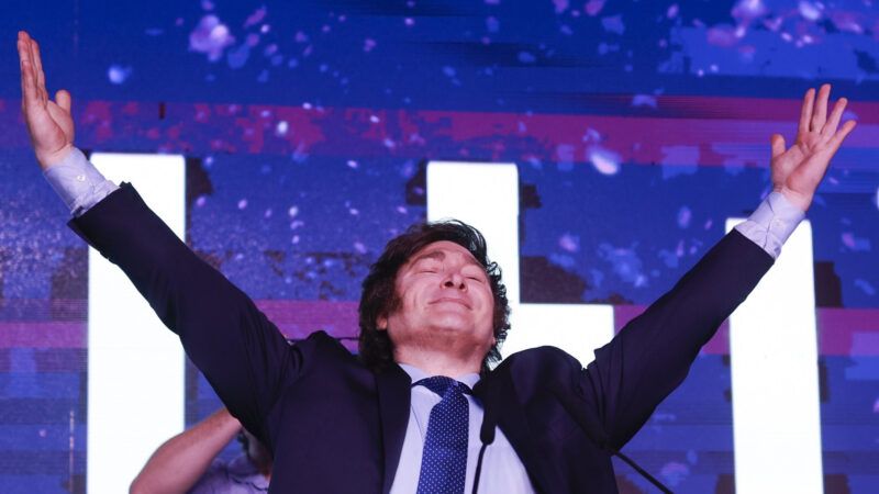 Javier Milei standing with his arms raised in the air in front of a purple background. | Anibal Greco/Newscom