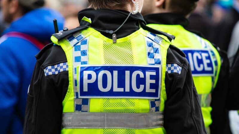 A British police officer wears a yellow vest with "POLICE" on the back. | Wirestock | Dreamstime.com