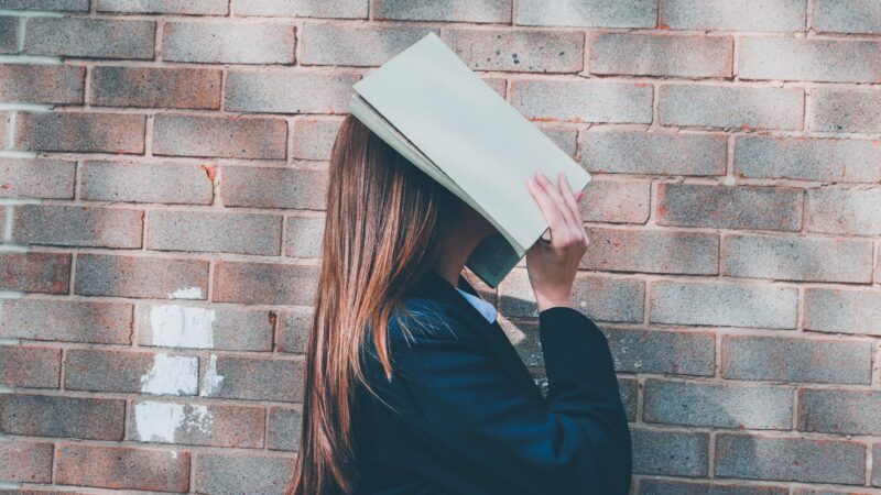 high school girl with book over her face | Photo by <a href=https://reason.com/2023/08/04/florida-effectively-banned-ap-psychology-with-rules-against-teaching-about-gender-sexual-orientation/