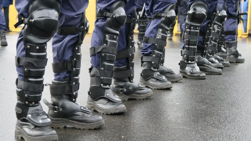 A line of police officers in riot gear, seen from the knees down. | Kalvis Kalsers | Dreamstime.com