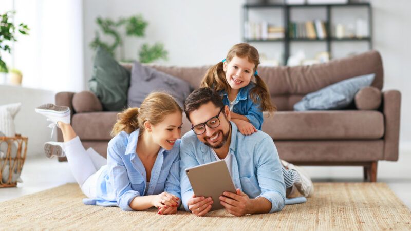 A father, mother, and little girl happily look at a tablet. | Evgenyatamanenko | Dreamstime.com