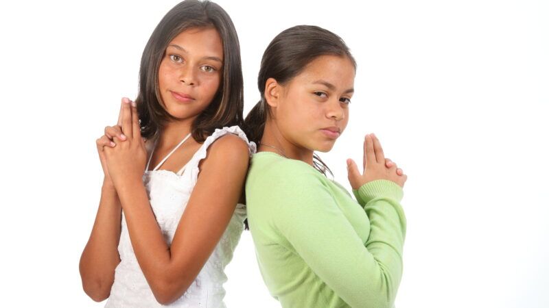 Two girls stand back to back, holding their fingers like guns. | Darrinhenry | Dreamstime.com