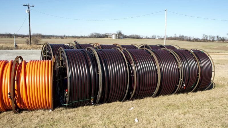 Large drums of fiber optic cable sitting in a field, with a barn and silo in the background. | Sherry Young | Dreamstime.com