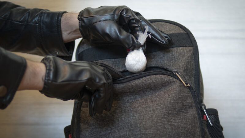A gloved individual holds a baggy of drugs outside a backpack, as if they are either planting or removing the baggy. | Dmitrii Melnikov | Dreamstime.com
