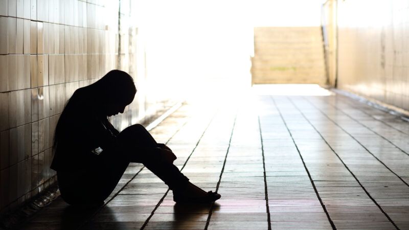 A sad teenager sits against the wall in a darkened hallway with head down. | Antonio Guillem | Dreamstime.com