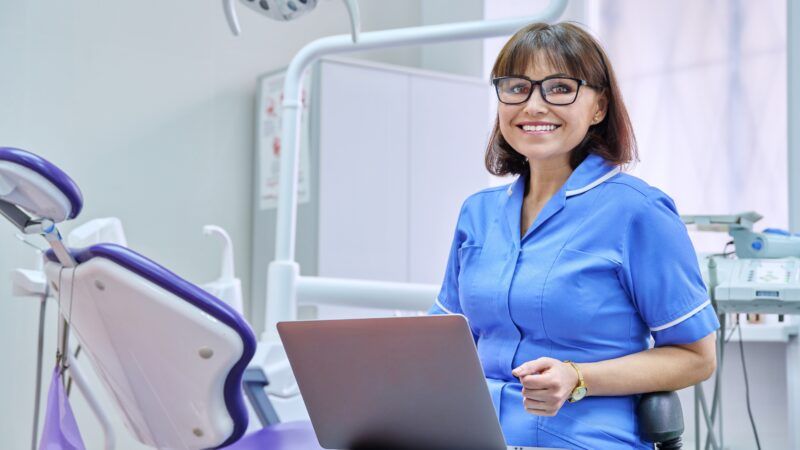 A female dentist sits by the patient's chair with a laptop open. | Valerii Honcharuk | Dreamstime.com