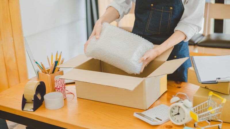 A woman packs a bubble-wrapped item into a box for shipping from her home business. | Atit Phetmuangtong | Dreamstime.com
