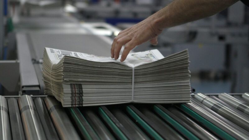 A hand reaches down to grab a bundle of newspapers bound with twine. | blurf | Dreamstime.com
