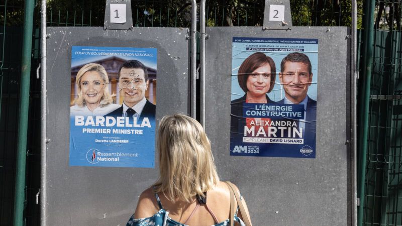 A woman stands in front of two campaign posters for France's parliamentary elections. | SYSPEO/SIPA/Newscom