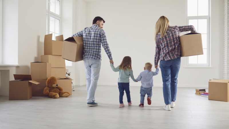 A young family, with father, mother, and two small children, carry boxes into a new apartment. | Lacheev | Dreamstime.com 