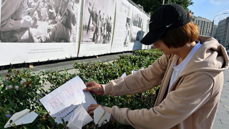 Person holding a white piece of paper that says FREE DUROV next to paper airplanes stuck in a bush. | Kommersant Photo Agency/Kommersant/Newscom