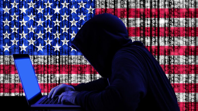 A shadowy hacker, in a hood, working on a laptop against the backdrop of an American flag, partially rendered in streams of binary code. | DPST/Newscom