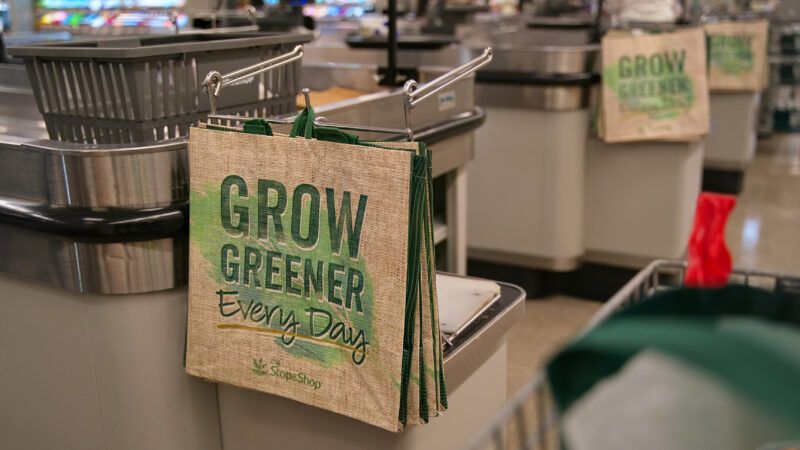 A rack of reusable grocery bags that say "GROW GREENER EVERY DAY," in a supermarket checkout line. | Rtdeleon04 | Dreamstime.com