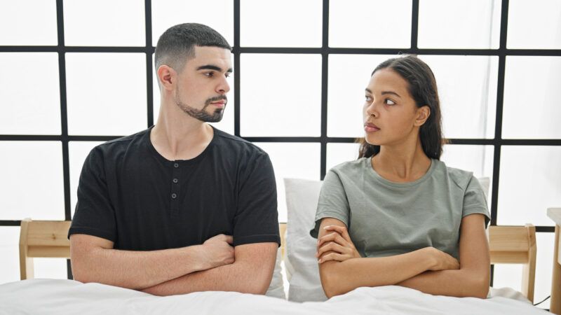 Attractive young interracial couple in bed, with arms folded, glaring at one another. | Aaron Amat | Dreamstime.com