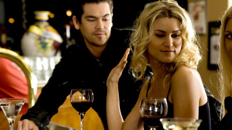 An attractive blonde woman at a bar holds up her hand and turns away from a man, indicating she is not interested. | Dreamstime Agency | Dreamstime.com