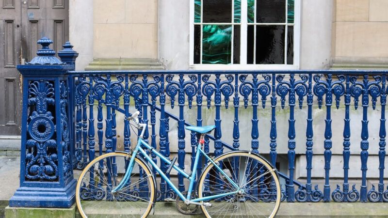 A light blue bicycle leans against a dark blue iron railing in Glasgow, Scotland. | Erin Donalson | Dreamstime.com