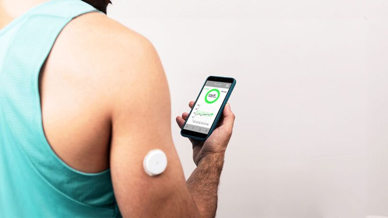 A person wearing a glucose monitor linked to a smartphone | Photo: Jesus Rodriguez/iStock