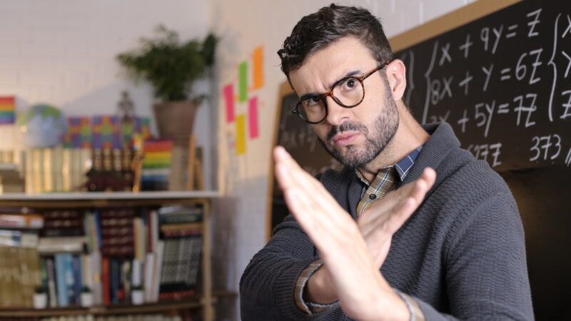 A teacher in a classroom holds his hands up in a karate stance. In the background, math problems are written on a chalkboard. | Alberto Jorrin Rodriguez | Dreamstime.com