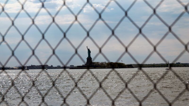 The Statue of Liberty as seen in the distance through a chain link fence. | Willeye | Dreamstime.com