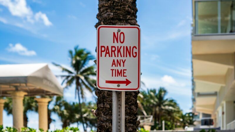 A sign that reads "No Parking Any Time," with an arrow, attached to a palm tree. | Wirestock | Dreamstime.com