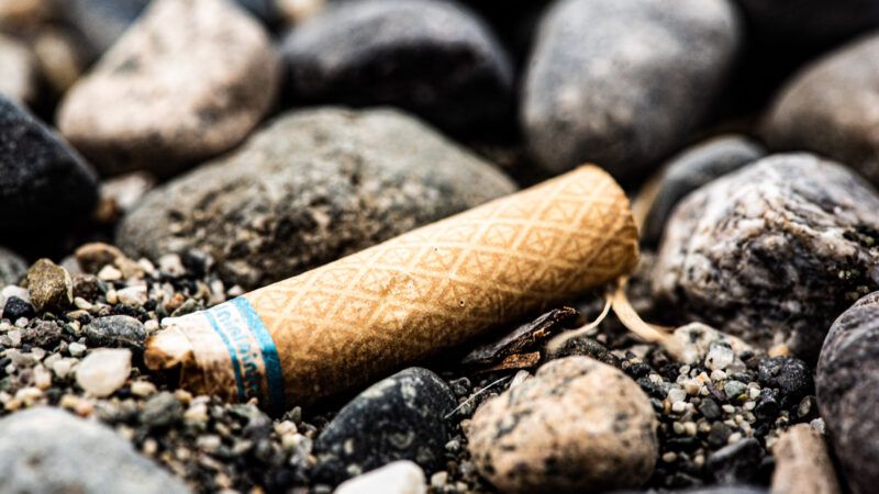 A discarded cigarette butt, among rocks and sand, as if on a beach. | Jonathanvaldez | Dreamstime.com