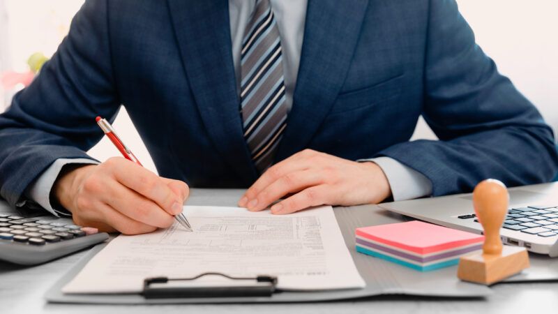 A businessman, wearing a suit, fills out a tax form on a clipboard. | Piotr Adamowicz | Dreamstime.com