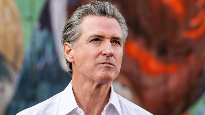 California Gov. Gavin Newsom stands in front of a multi-colored wall | Hector Amezcua/TNS/Newscom