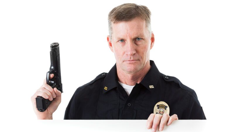 A white man in a police officer's uniform, holding a handgun, peers over a white barrier, against a white backdrop. | Seanlockephotography | Dreamstime.com