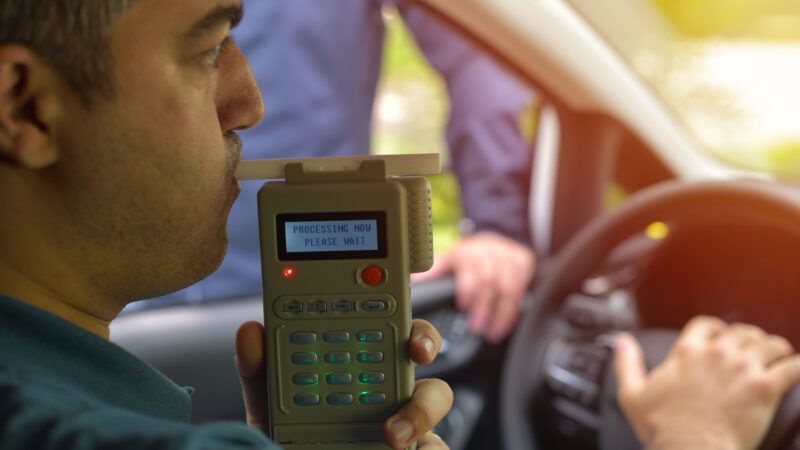 A man behind the wheel of a car blows into a breathalyzer. | Daniel Chetroni | Dreamstime.com