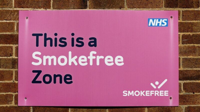 Pink sign on a brick wall that reads "This is a Smokefree Zone." There is a National Health Service (NHS) logo in one corner and a SmokeFree logo in another corner. | Peter Fleming | Dreamstime.com