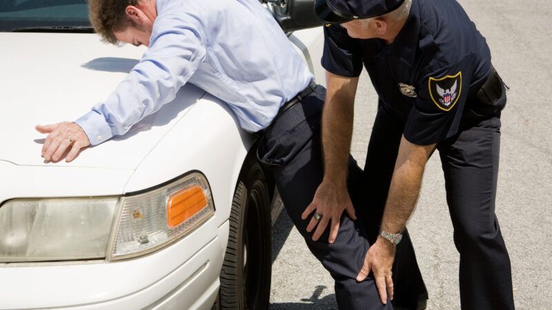 A police officer searches a man during a traffic stop, feeling the inside of his leg. | Brian T. Young | Dreamstime.com