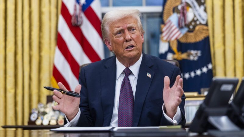 President Donald Trump sits at the Resolute Desk in the Oval Office, holding a pen in one hand as if in the process of signing an executive order. | Jim LoScalzo - Pool via CNP/Polaris/Newscom