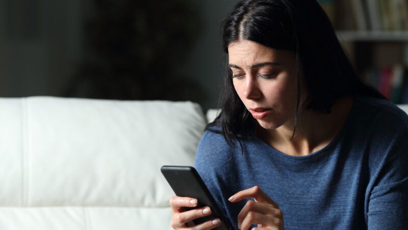 A brunette woman looks at her cell phone with concern. | Antonio Guillem | Dreamstime.com