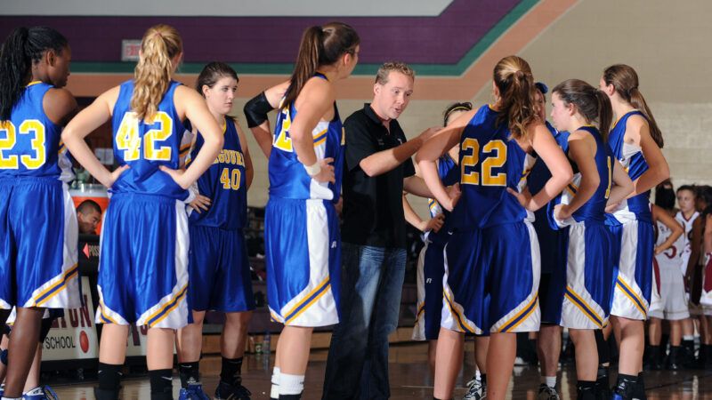 A girls' basketball team in uniform listens to their male coach. | Mbr Images | Dreamstime.com