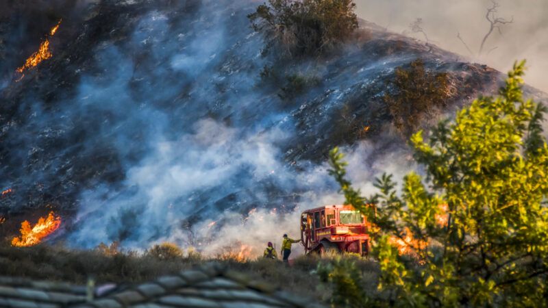 Firefighters stand near a bulldozer as fire burns on a hillside. | Erin Donalson | Dreamstime.com