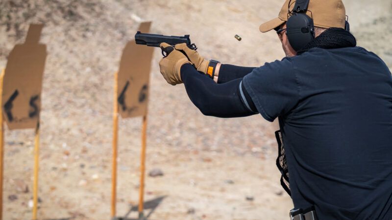 A man wearing gloves and earmuffs fires a pistol at a firing range. | Svetlana Day | Dreamstime.com