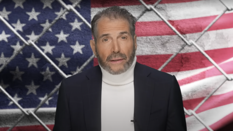 John Stossel is seen in front of an American flag and a chain-link fence | Stossel TV