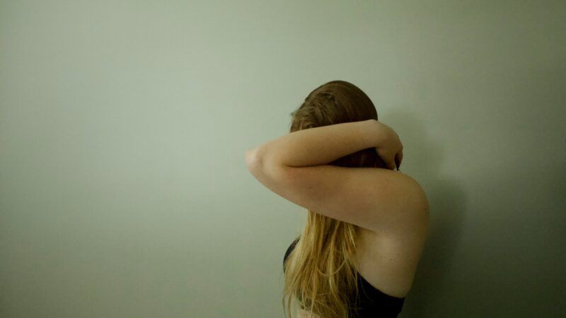 A photo of a woman in a bra obscuring her face with her arm | Photo by <a href="https://unsplash.com/@addymae?utm_content=creditCopyText&utm_medium=referral&utm_source=unsplash">Addy Mae</a> on <a href="https://unsplash.com/photos/a-woman-with-her-head-in-her-hands-leaning-against-a-wall-FNIrireBNGM?utm_content=creditCopyText&utm_medium=referral&utm_source=unsplash">Unsplash</a>       