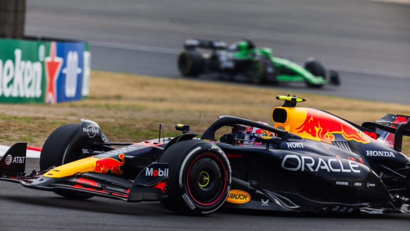 Side view of a Red Bull Racing F1 car going through a turn, with a green Stake F1 car in the background | Jay Hirano/AFLO/Newscom