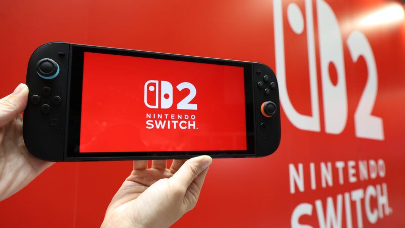 Hands hold a Nintendo Switch 2 console near a display with the logo on it, at an event. Hands hold a Nintendo Switch 2 console near a display with the logo on it, at an event. | Fumiyasu Nakatsuji/Jiji Press/Newscom