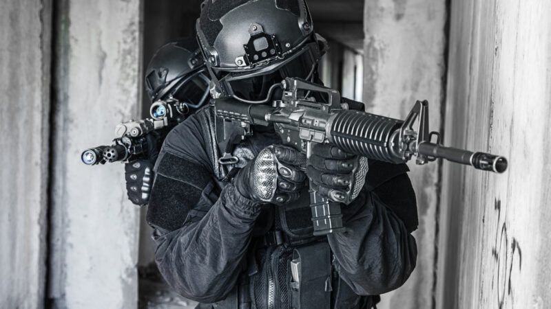 Police officers in SWAT gear holding automatic weapons, move through a building as if conducting a raid. | Oleg Zabielin | Dreamstime.com