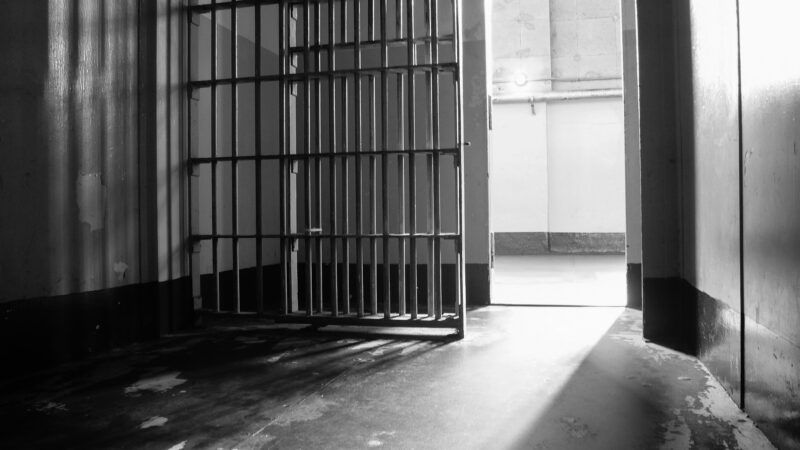 A black-and-white photo from inside a jail cell, with the cell door open. | Simon Campbell | Dreamstime.com
