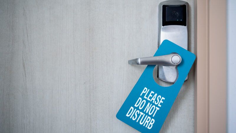 A closed hotel room door, with a blue sign on the handle that says "Please Do Not Disturb." | Ezthaiphoto | Dreamstime.com